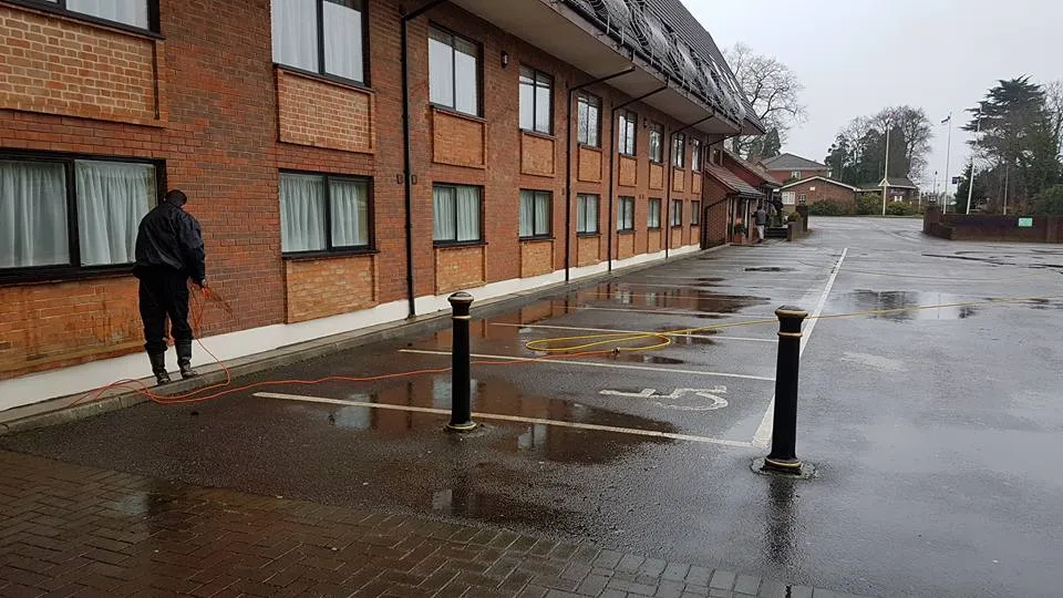 A man walking down a wet street next to a red brick building.